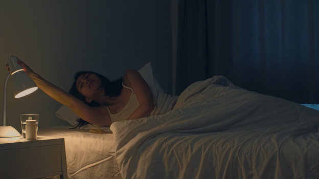 Молодая девушка выключает ночник и лежит в кровати