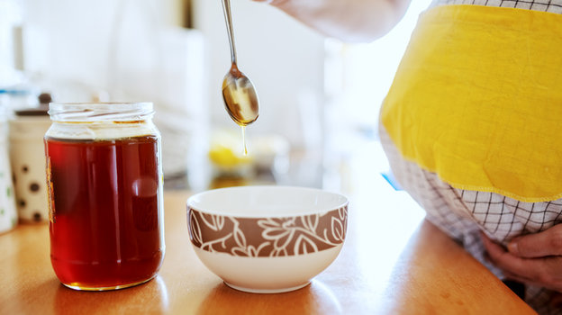 Беременная льет мед в миску.